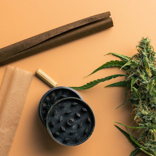 Nahaufnahme von Cannabisblüte, Grinder, Rolling Papers und Blunt Wrap auf beigem Hintergrund. Vorbereitungsmaterialien für den Cannabis-Konsum.